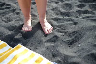 Low section of person standing at sandy beach