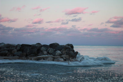 Rocks in sea against sky during sunset