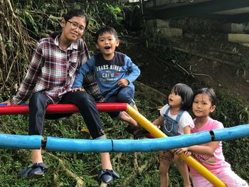 Portrait of happy siblings sitting on slide at playground