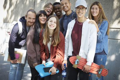 Portrait of smiling university friends standing against building in campus