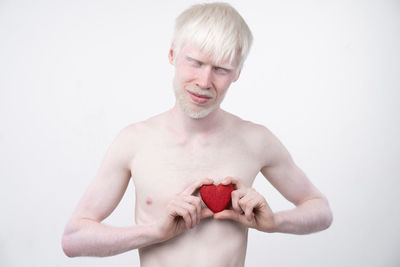 Shirtless man with albino holding heart shape against white background