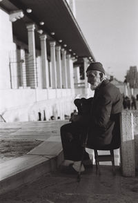 Side view of senior man sitting on chair in front of mosque