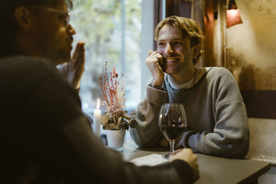 Happy gay man talking with boyfriend during candlelight date at restaurant