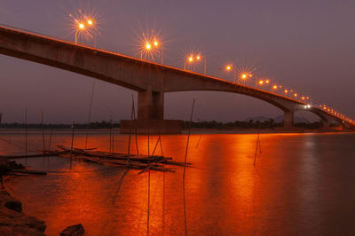 Illuminated bridge over river against sky at night
