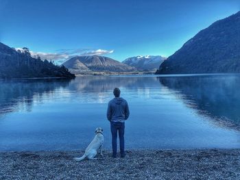 Rear view of man standing by lake against mountain range