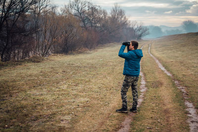 Full length of man looking through binoculars while standing on field