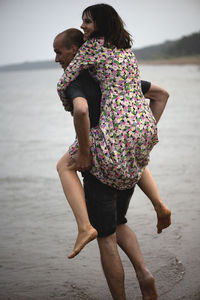 Young couple having fun on the beach at rainy summer day,a man carries a woman on his shoulders 
