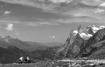 Rear view of people sitting on mountain against sky