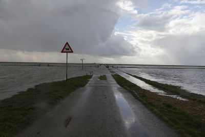 Road by calm sea against sky