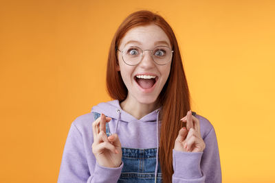 Woman with fingers crossed against yellow background