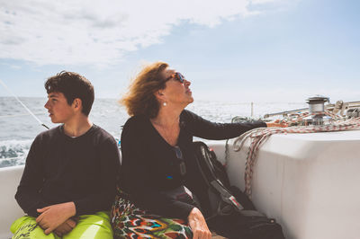 Mature woman by son sitting in boat on sea against sky