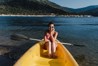Full length of woman in bikini sitting on boat in lake