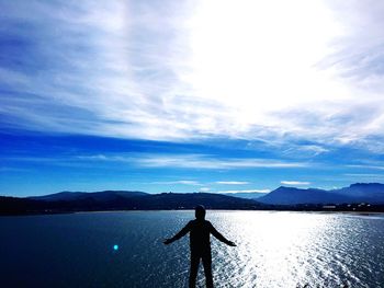 Rear view of man standing by lake against sky