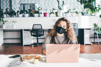 Freelancer woman wearing protective mask and using laptop at comfortable office. 