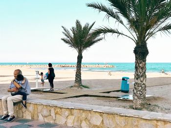 People sitting on beach by sea against sky