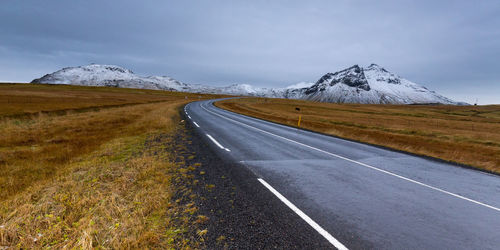 Empty road leading towards snowcapped mountains against cloudy sky