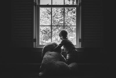 Girl with teddy bear by window at home