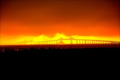 Silhouette cranes against orange sky during sunset