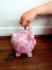 Midsection of woman holding pink flower on table against wall