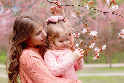 Mother and little girl in the park with blooming pink sakura