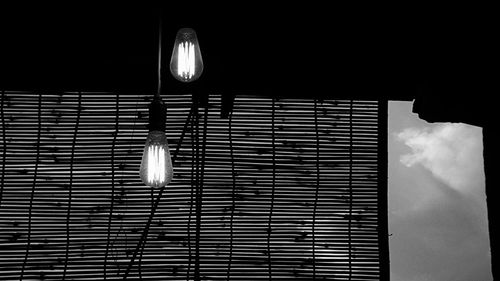 Low angle view of illuminated light bulbs against bamboo blinds