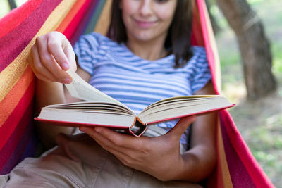 Tranquil female lying in hanging hammock in park and enjoying interesting book at summer weekend