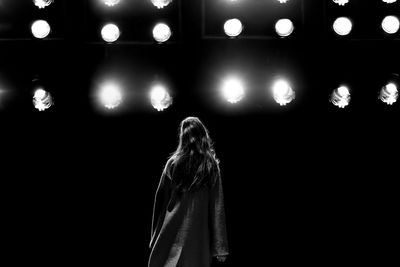 Rear view of woman standing against illuminated lights at night