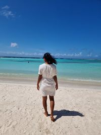 Rear view of boy standing on beach against sky