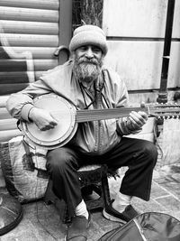 Man playing string instrument while sitting on footpath