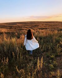 Woman in white coat walking in the field and watching sunset