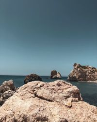 Rock formations by sea against clear blue sky