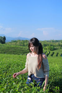 Contemplating woman picking leaves in tea plantation field against sky