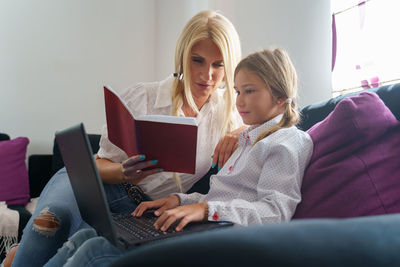 Young woman using phone while sitting on book