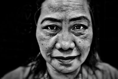 Close-up portrait of smiling senior woman against black background