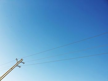 Low angle view of power lines against clear blue sky