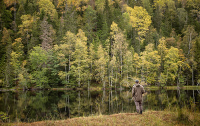 Man looking over a lake mirroring an autumn coloured forest