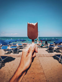 Cropped hand holding popsicle at beach against blue sky