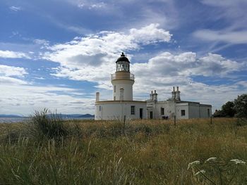 Lighthouse on field by building against sky