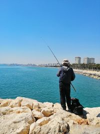 Rear view of man fishing in sea against sky