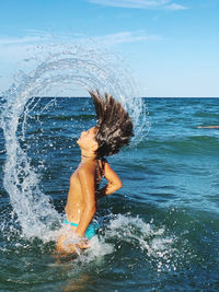 Girl splashing water in sea against sky