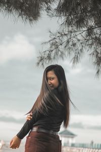 Young woman standing by tree against sky