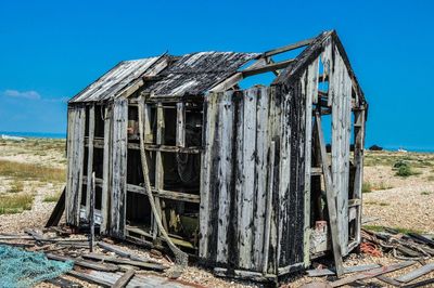 Old damaged wooden house on field against blue sky during sunny day