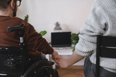 Man in wheelchair holding girlfriend's hand at home