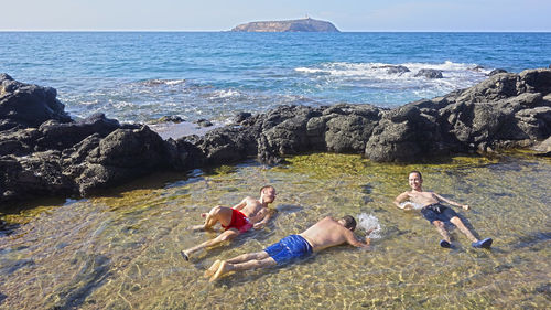 High angle view of men relaxing in water at beach against sky