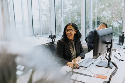 Cheerful senior businesswoman sitting at computer desk while looking away in office