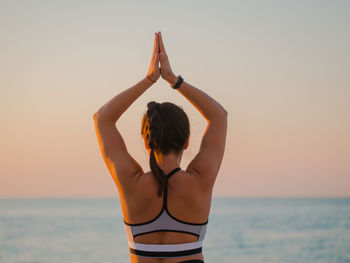 Rear view of woman standing at beach against sky during sunset