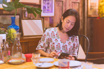 Woman looking at cell phone while sitting on table in restaurant