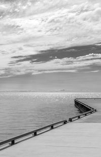 Black and white - a cement pier, dock, juts out from the corner into the sea/ocean 