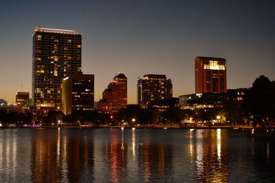 Illuminated buildings by river against sky in city at night