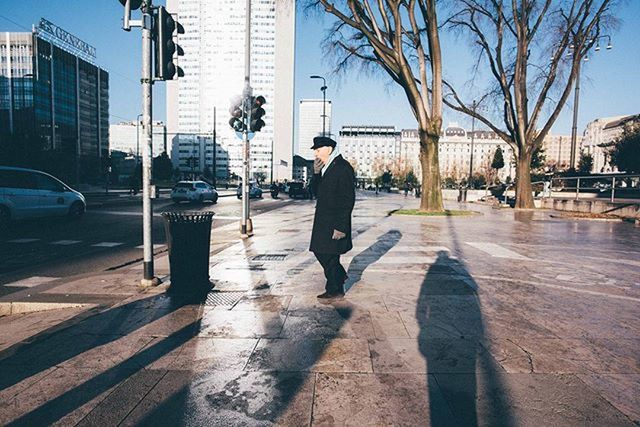 building exterior, city, architecture, transportation, built structure, street, city life, car, bare tree, mode of transport, road, walking, land vehicle, full length, men, lifestyles, tree, sidewalk